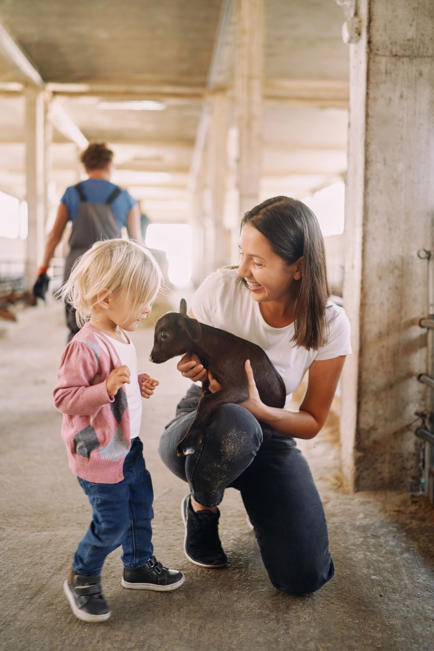 Smiling mother showing little girl a brown goatling